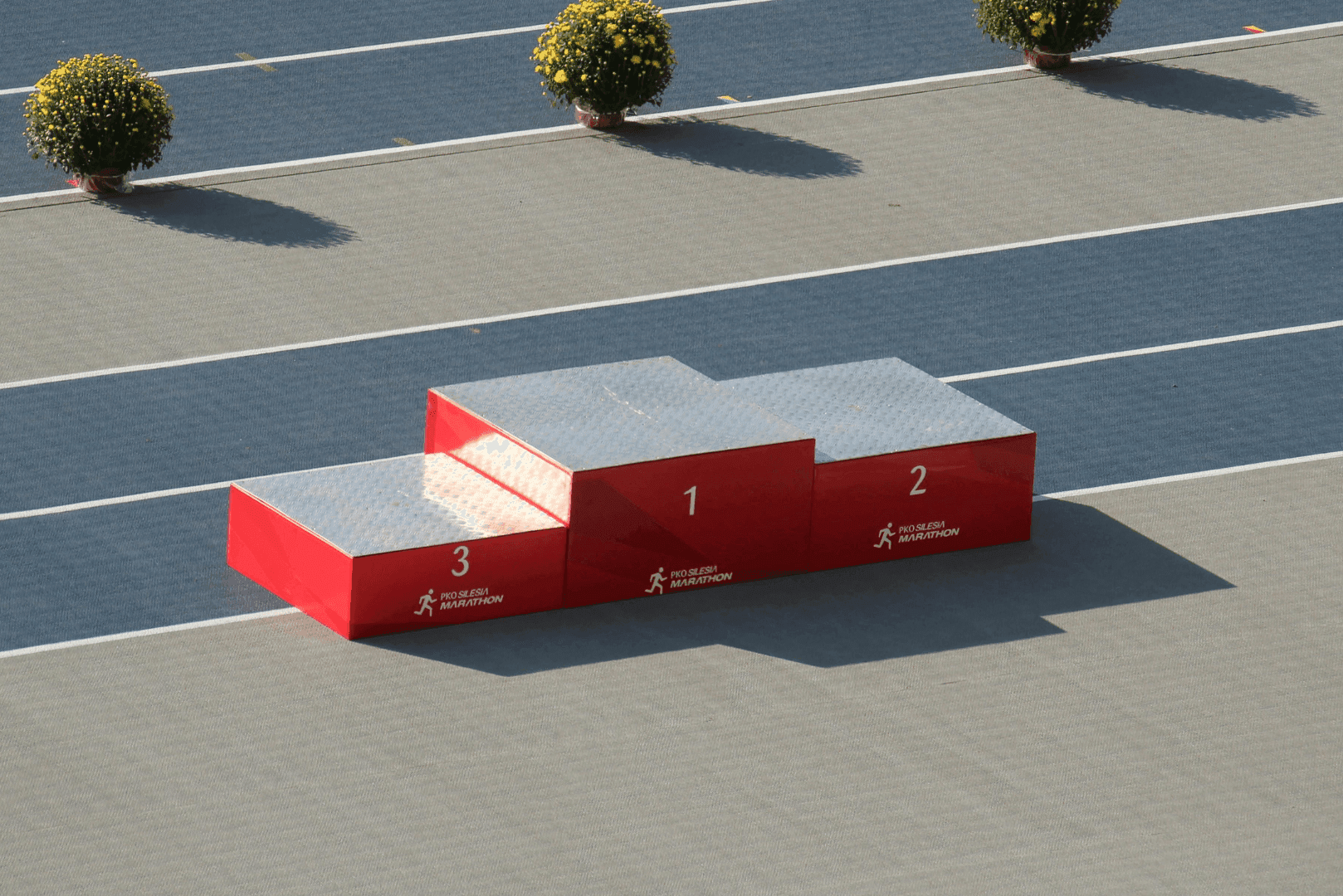 Puste podium sportowe z numerami 1, 2 i 3 na niebieskiej bieżni lekkoatletycznej – symbol przegranej walki o czołowe miejsca w rankingach lokalnych.