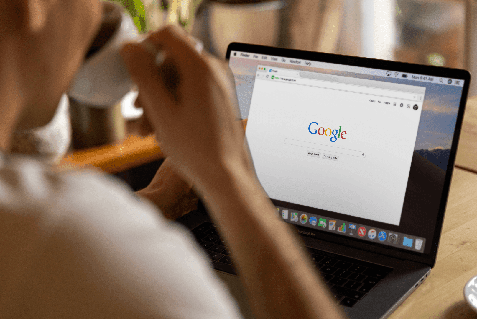 Osoba pijąca kawę i patrząca na ekran laptopa z wyświetloną wyszukiwarką Google – ilustracja problemów z widocznością w przeglądarkach.
