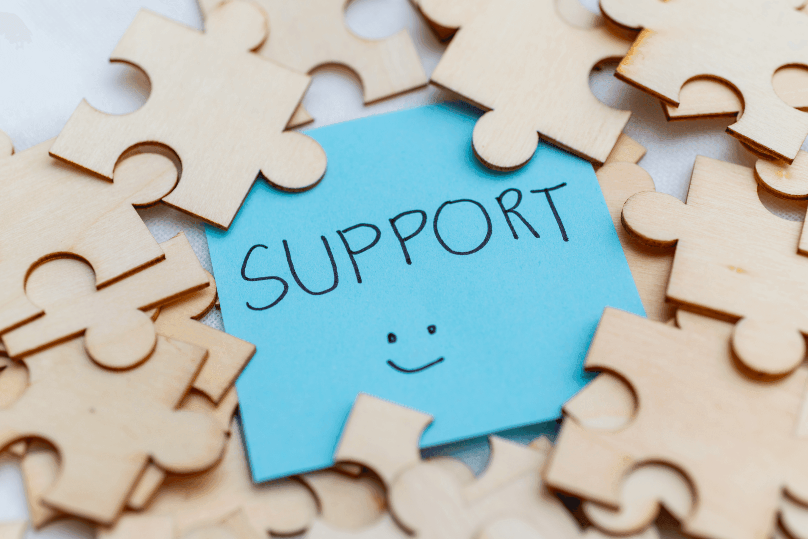Niebieska kartka z napisem SUPPORT i uśmiechniętą buźką, otoczona jasnymi puzzlami – wizualizacja osobistego wsparcia technicznego 1:1.