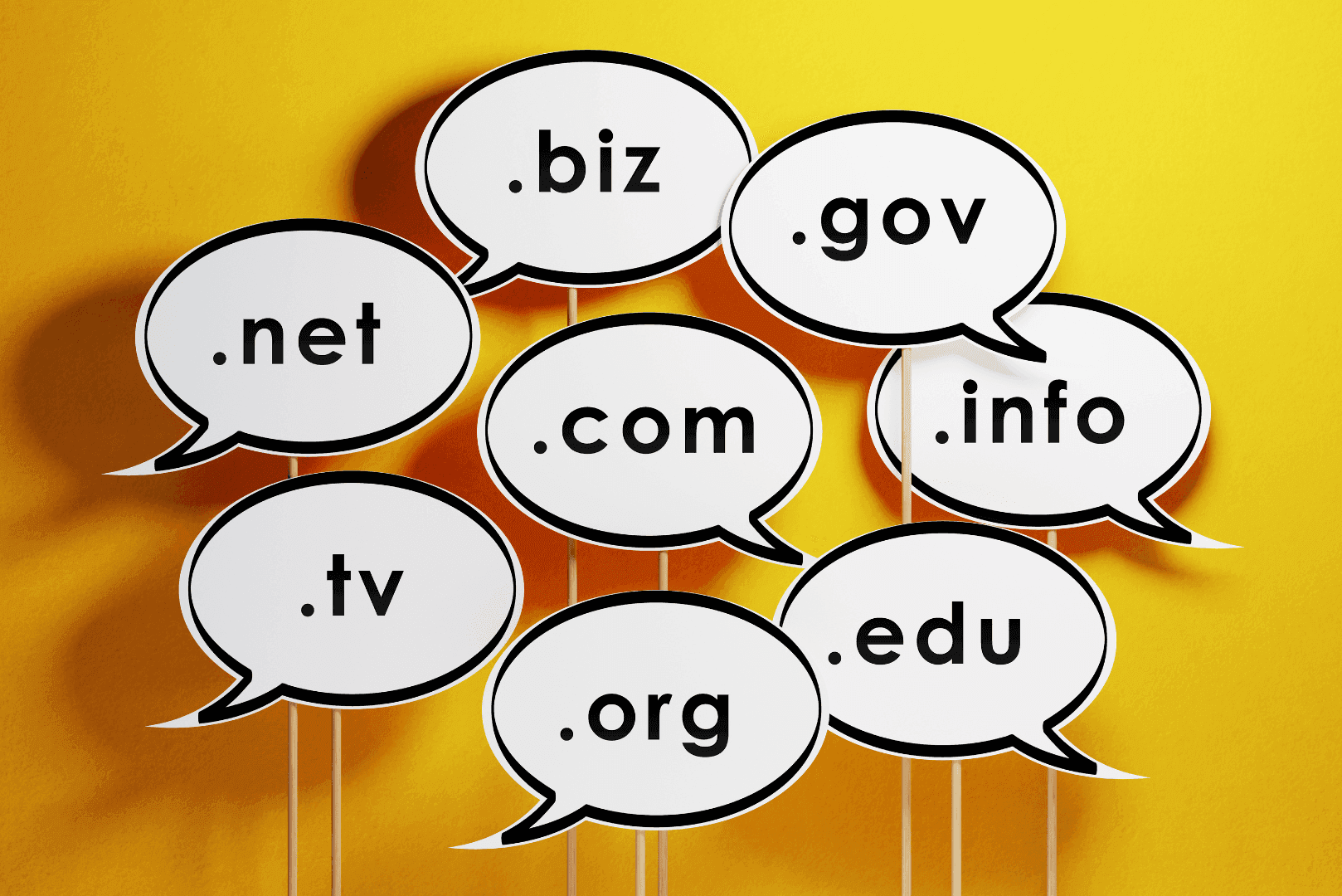 Osiem białych dymków dialogowych z nazwami rozszerzeń domen, m.in. .com, .net, .org, .biz na żółtym tle.