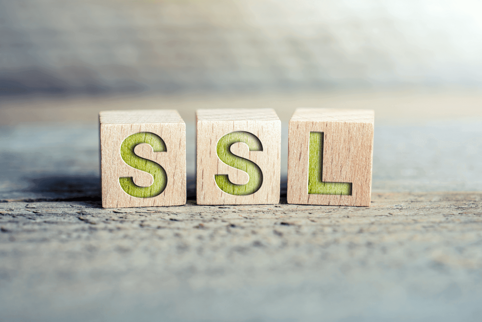 Trzy drewniane klocki z literami tworzącymi napis SSL, ustawione na rozmytym, jasnym tle – symbol bezpiecznego wizerunku z certyfikatem.